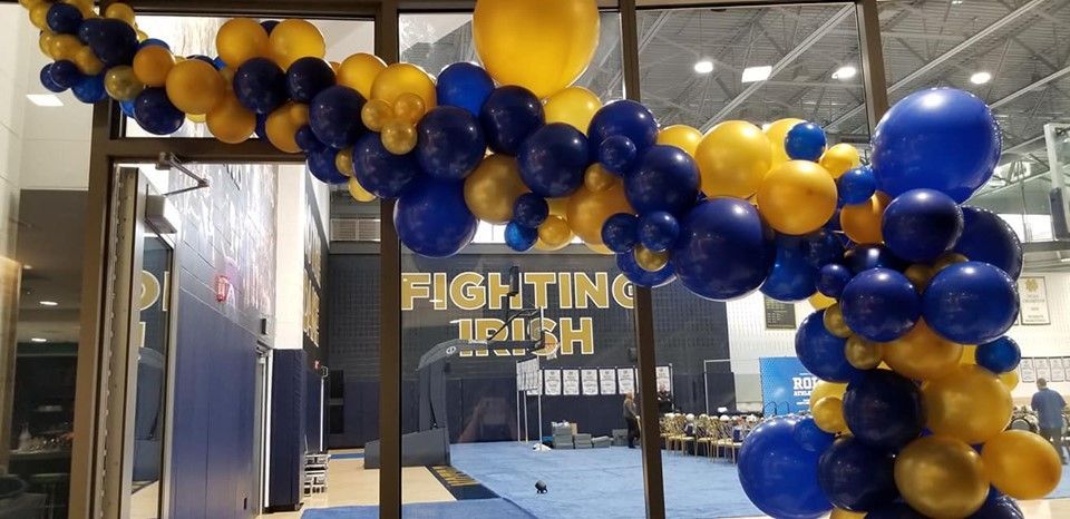 A garland of blue and yellow balloons are hanging from a window.