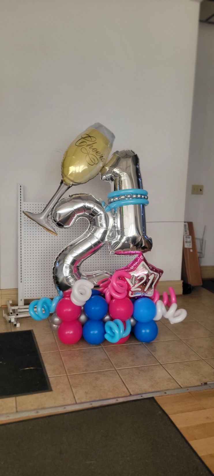 A balloon arrangement for a 21st birthday, with silver numbers, a champagne glass, and a blue, pink base.