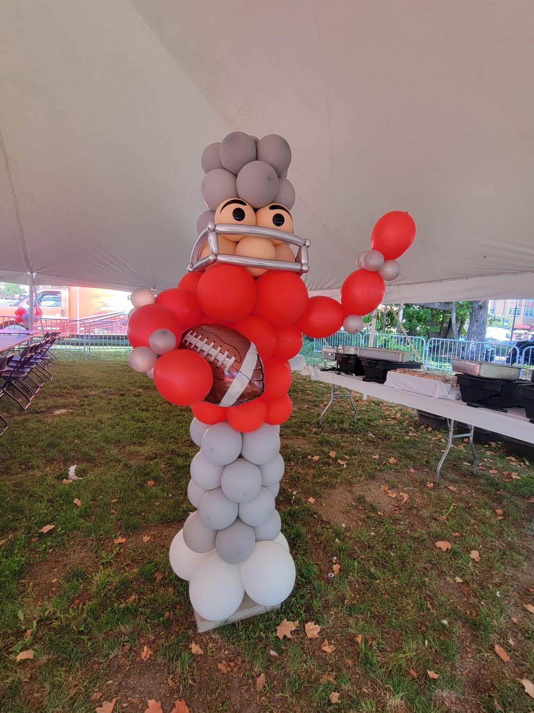 A football player made out of balloons is holding a football and wearing a helmet.
