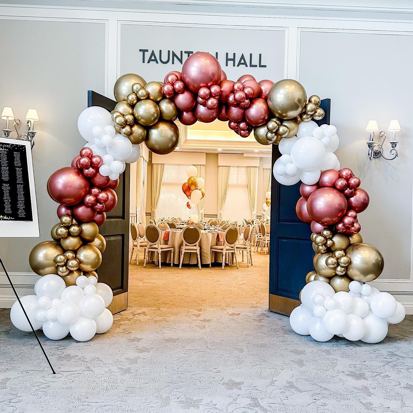 Balloon arch over doorway to event hall with gold, white and rose gold balloons.