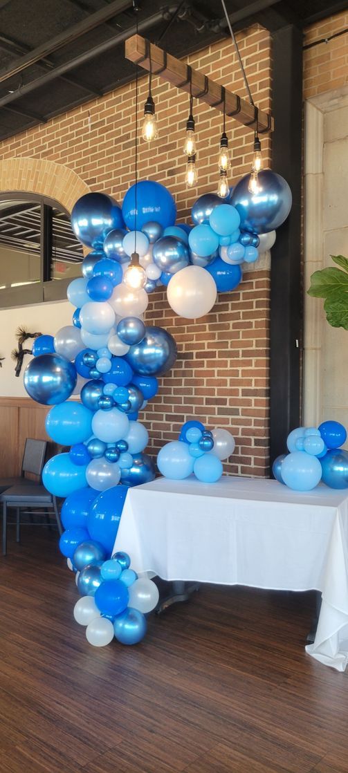 Blue balloon arch and table decoration at a brick wall with hanging lights.