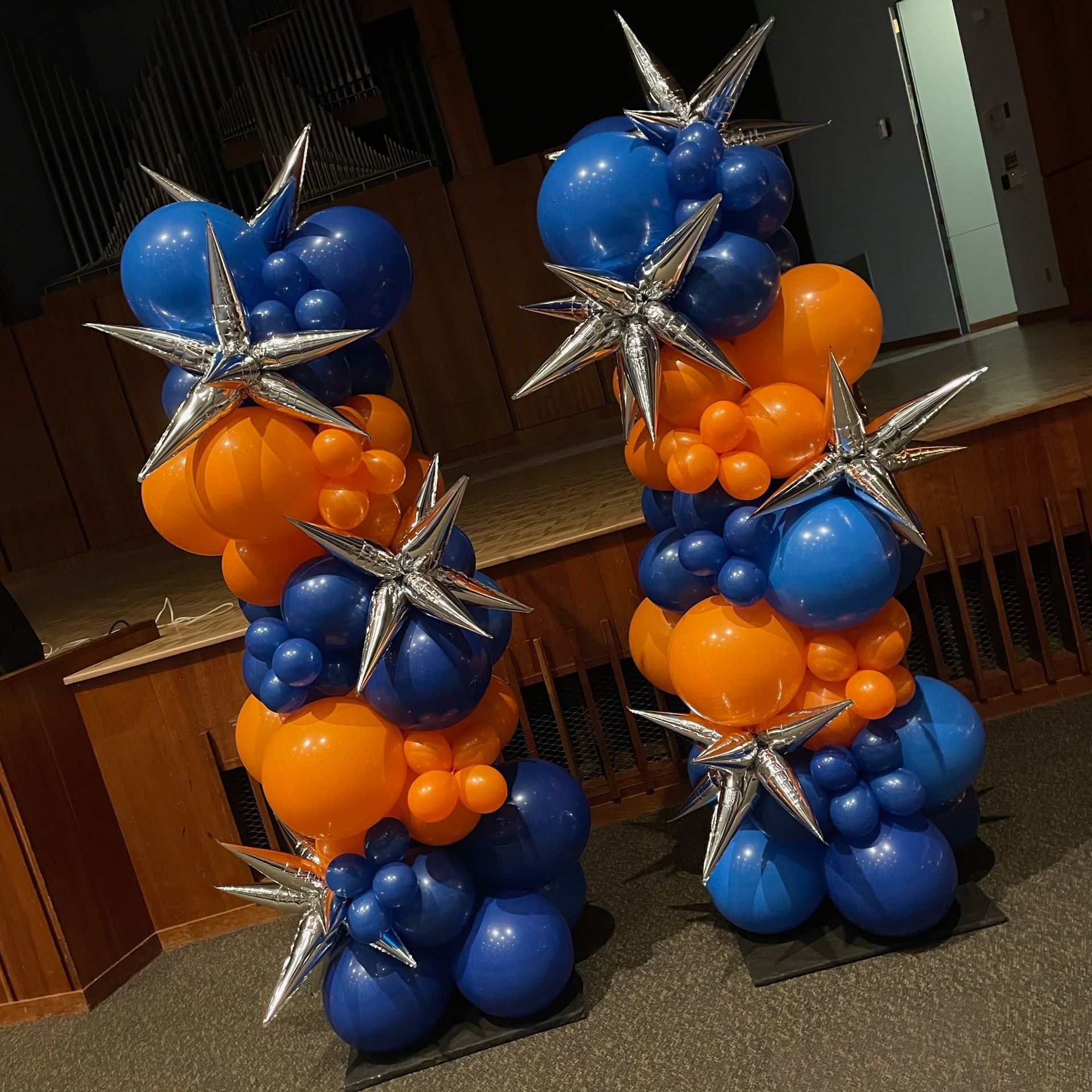 Two balloon columns with blue, orange, and silver starburst accents. Indoors.