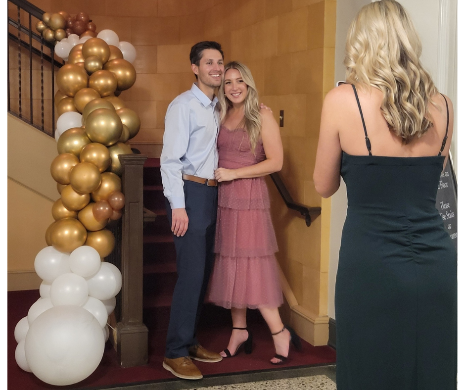 A woman is taking a picture of a man and woman in front of balloons