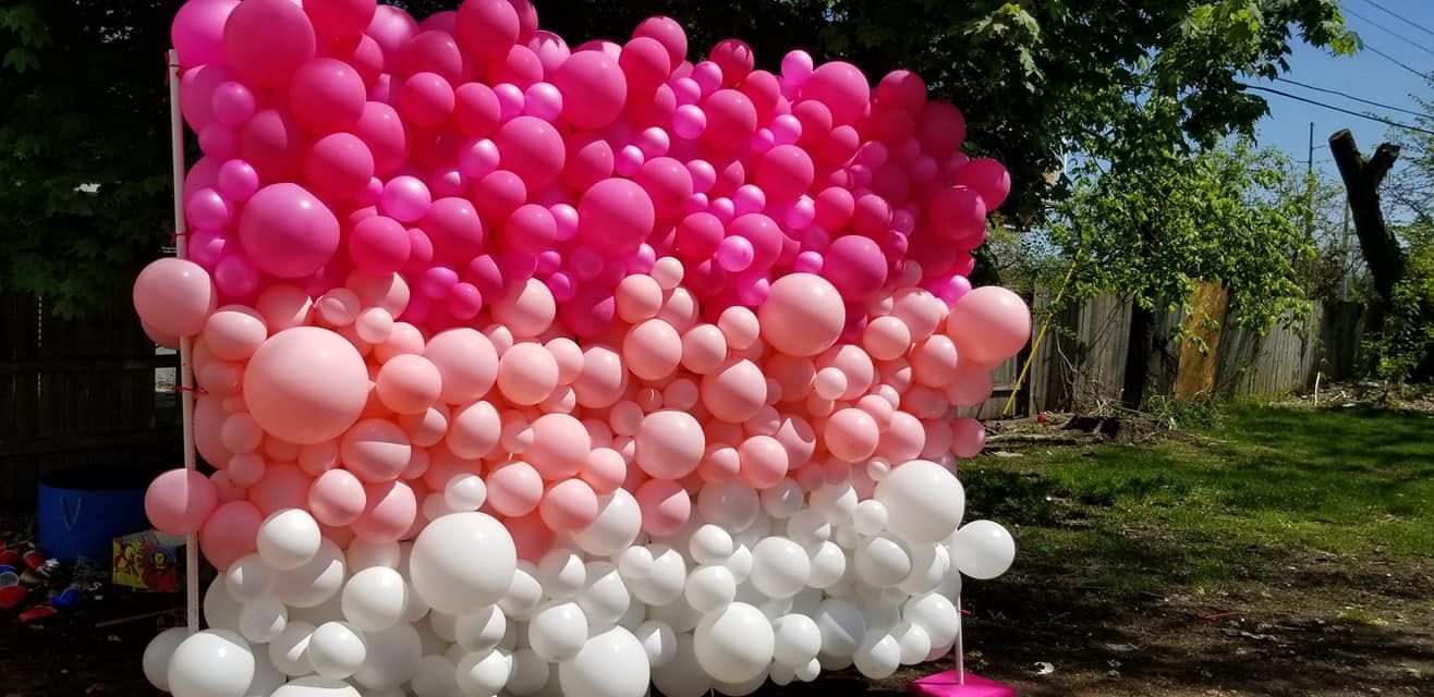 A wall of pink and white balloons in a park.