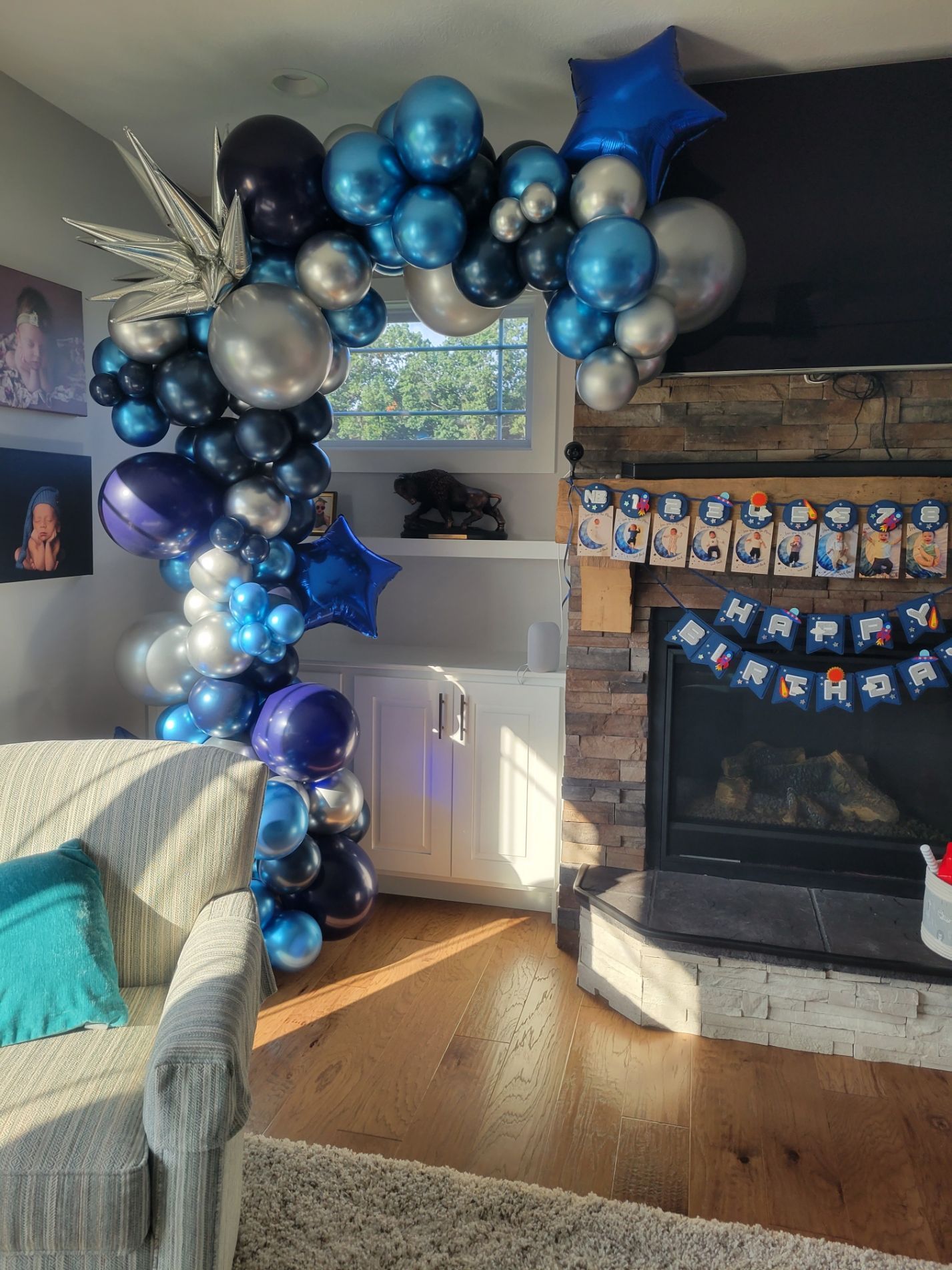 Balloon arch in shades of blue and silver, celebrating a birthday, next to a fireplace.