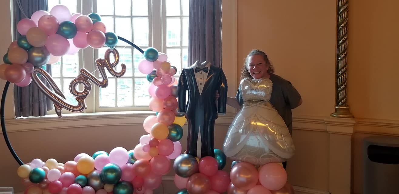 A woman is standing next to a bride and groom statue made of balloons.