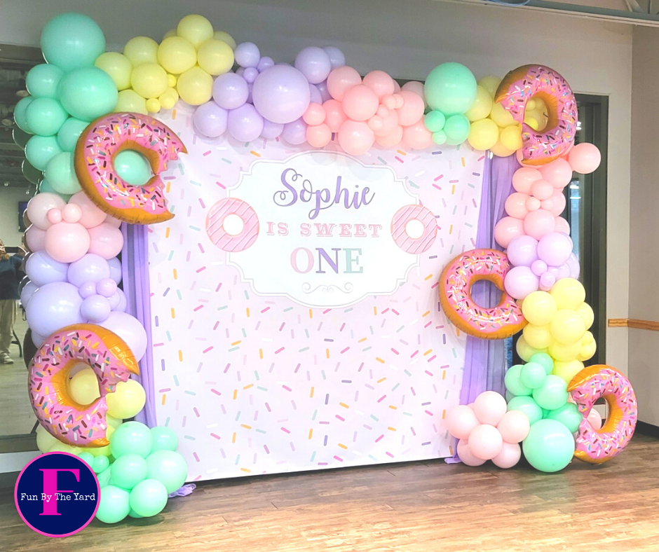 Donut-themed party backdrop with pastel balloons and inflatable donuts. Celebratory setup for 