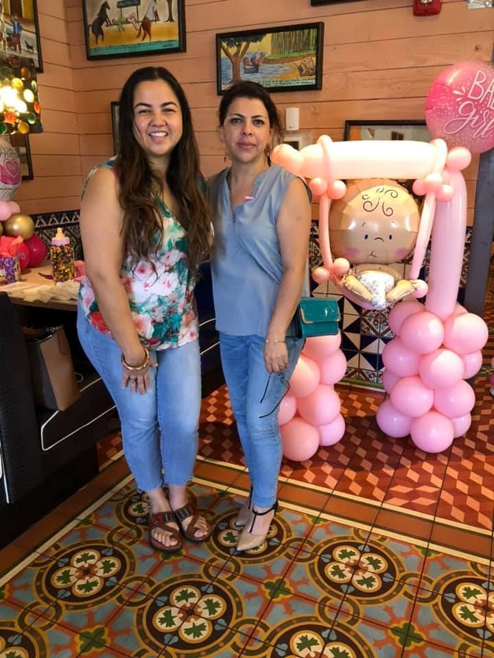 Two women are posing for a picture in front of a baby swing made of balloons.
