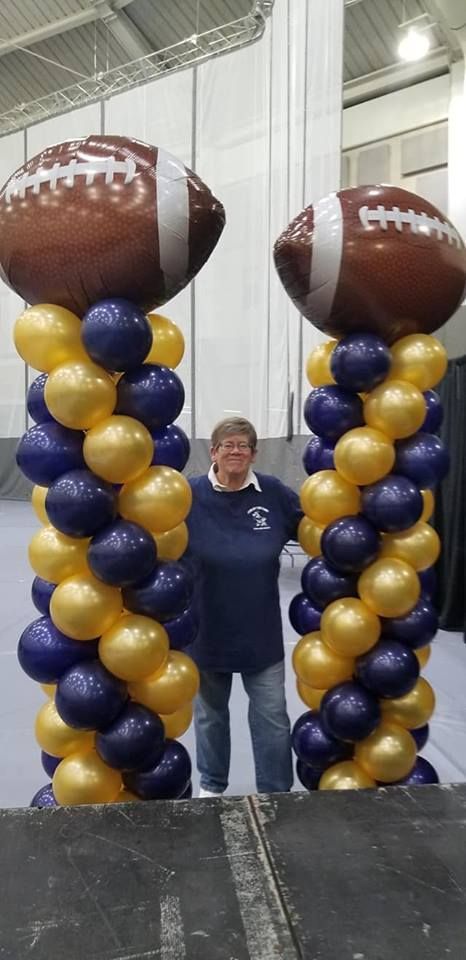 A woman is standing in front of two columns of balloons shaped like footballs.