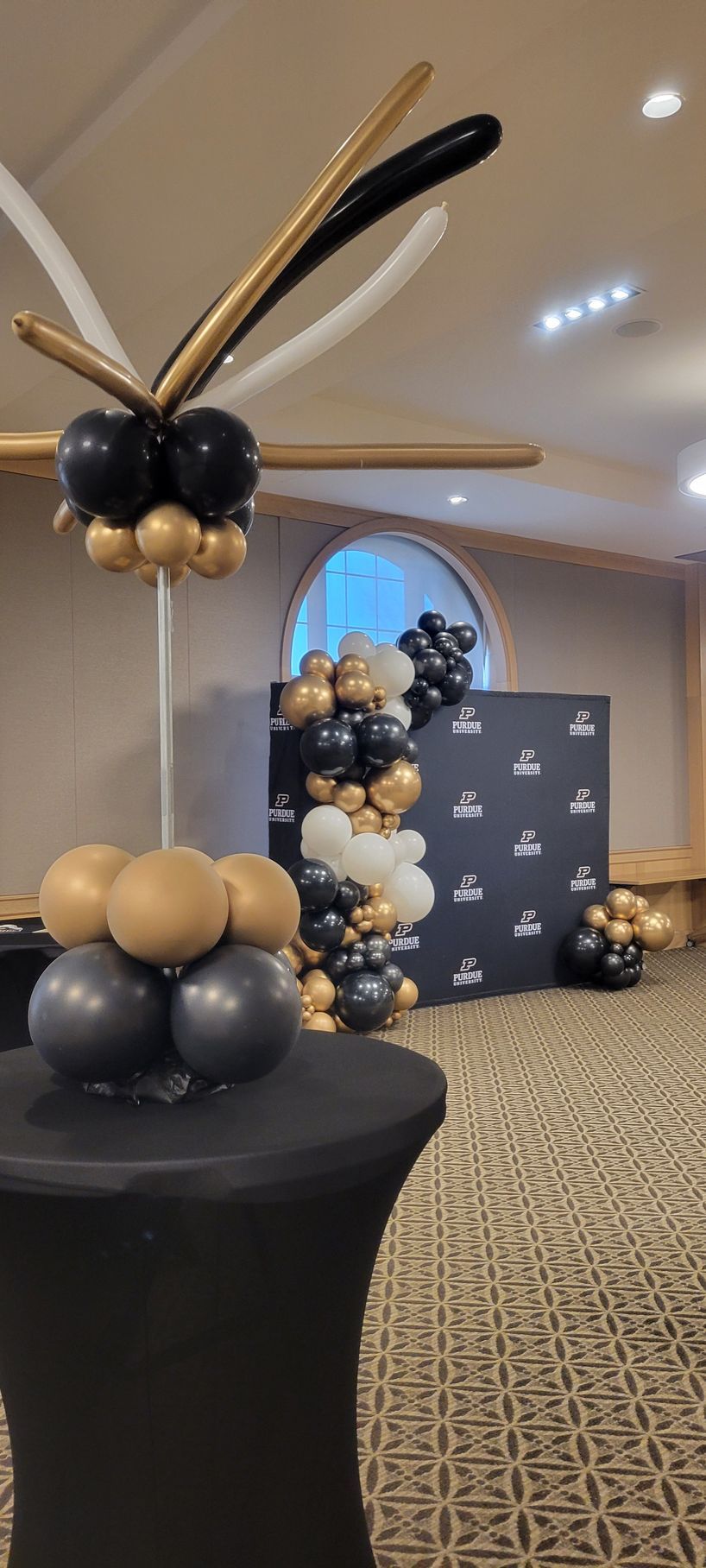 Event decor with black, gold, and white balloons. Tables and a backdrop are also adorned with balloons.