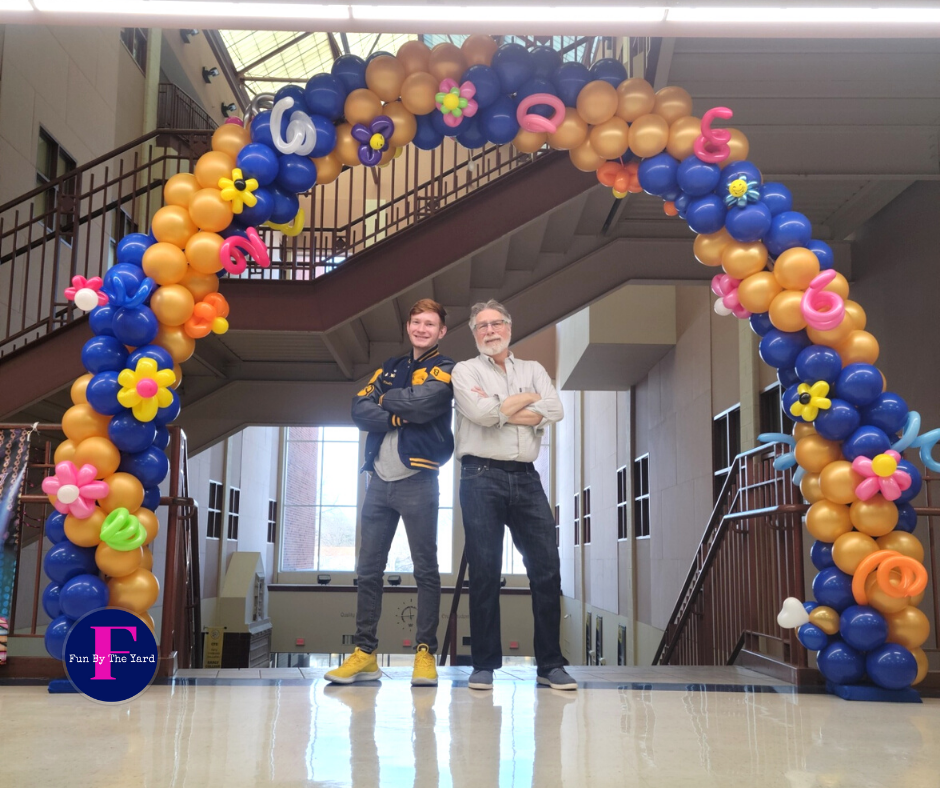 Two men are standing in front of a large balloon arch at Riley High School in South Bend
