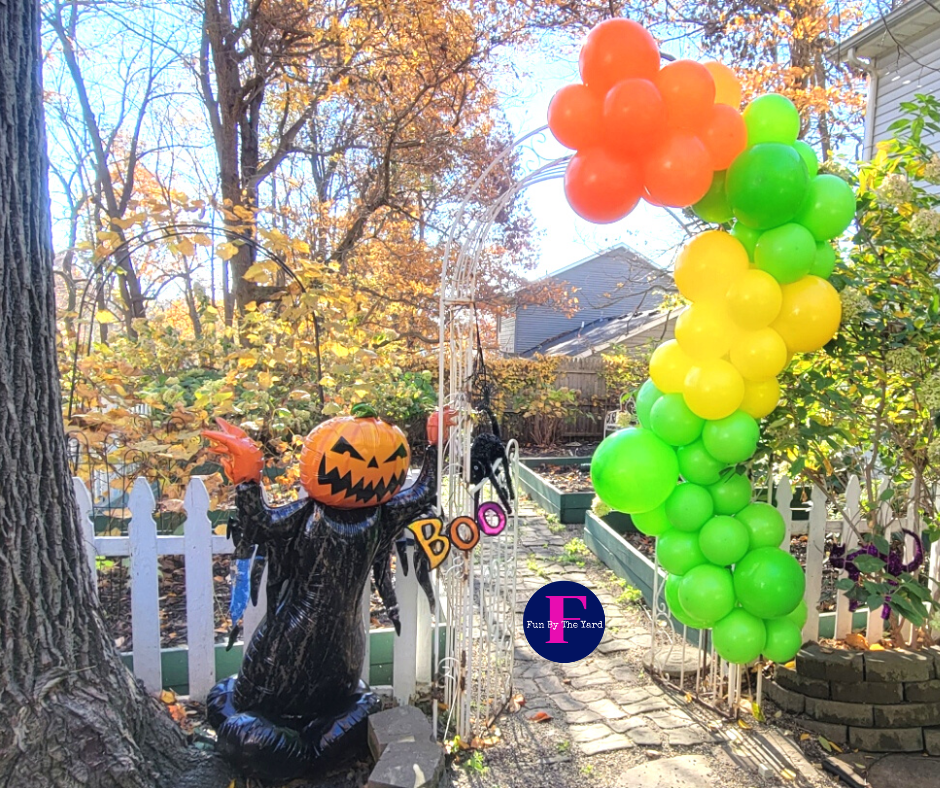 A ghost made out of balloons is sitting next to a tree in a yard.