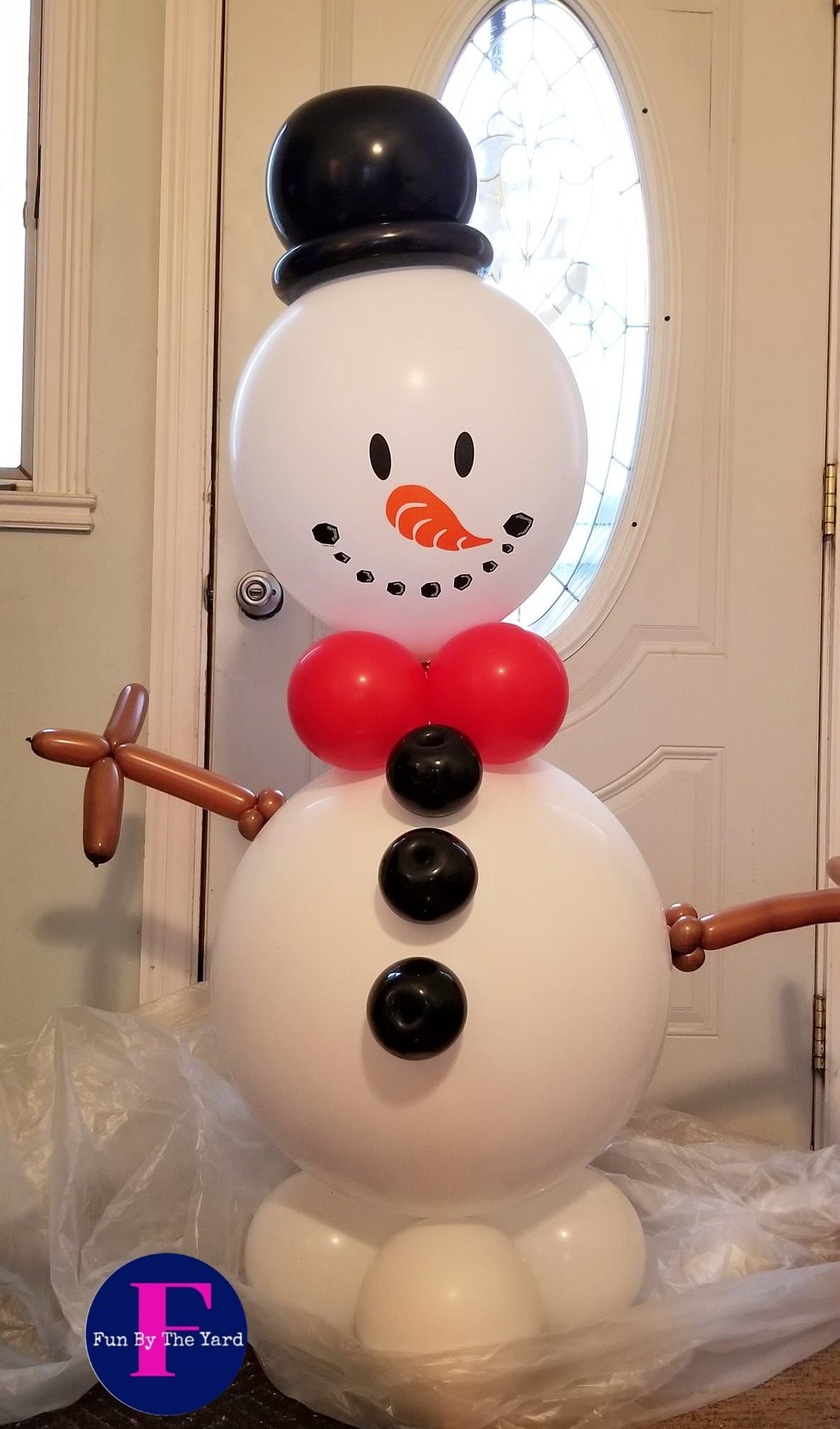 A snowman made out of balloons is standing in front of a door.
