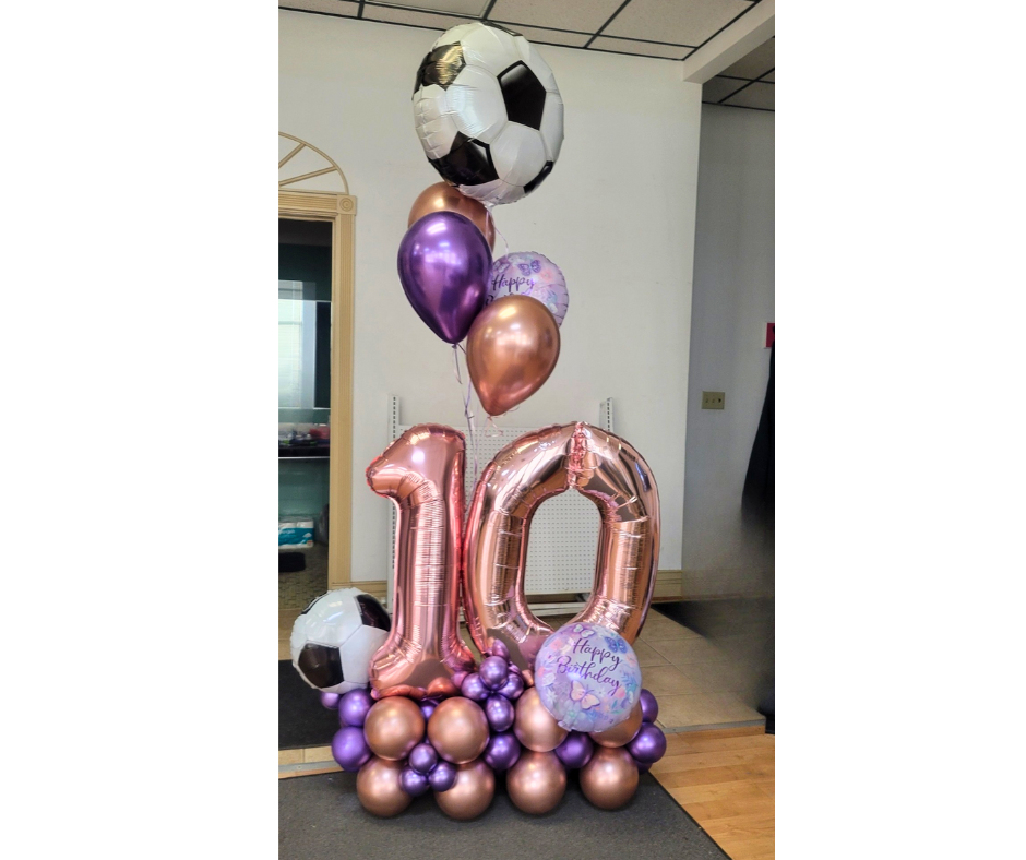 Soccer-themed balloon arrangement celebrating a 10th birthday: rose gold numbers, soccer balls, and purple balloons.