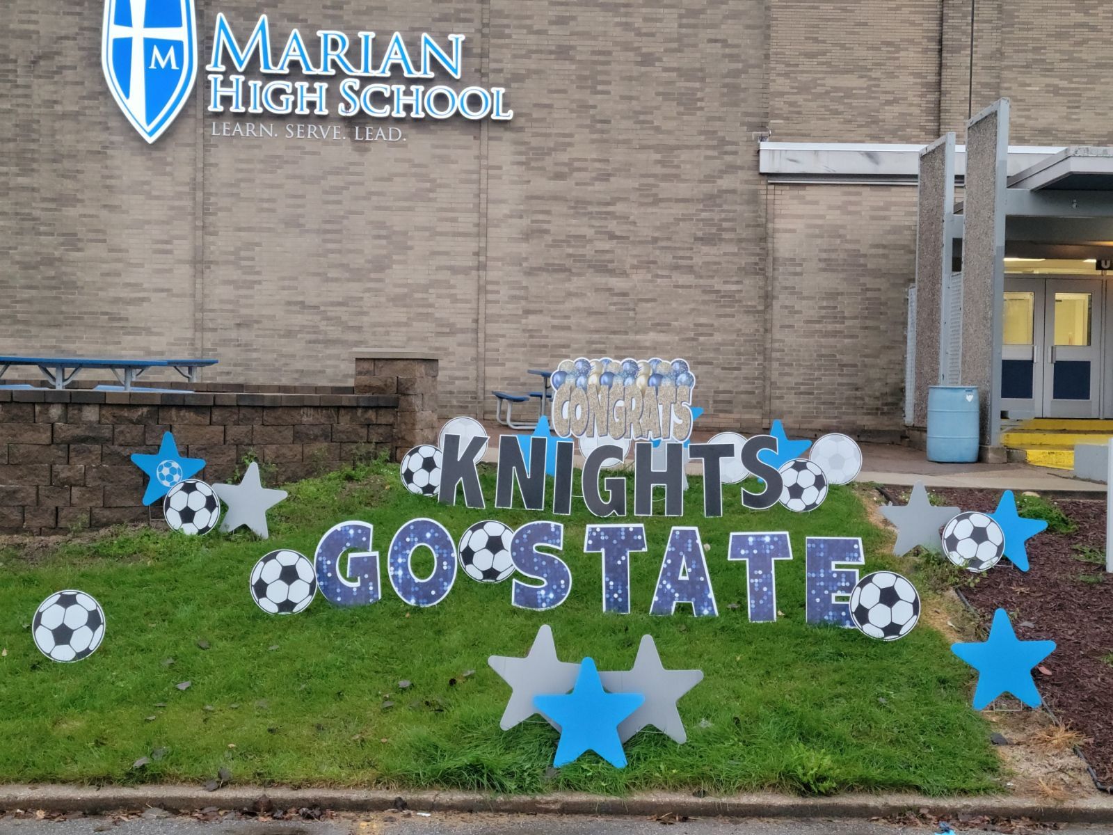 A sign in front of a building that says knights go state. Soccer themed yard card.