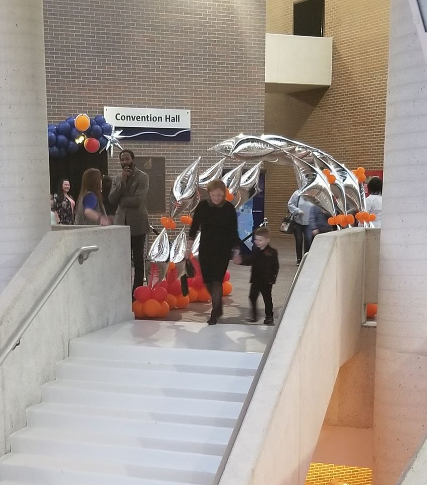 People are walking down stairs in a convention hall under a balloon tunnel