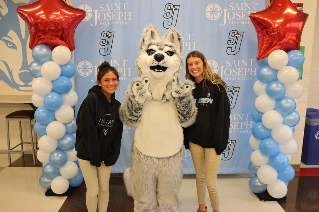 Blue and white balloon columns with red star toppers.  St Joe High School students with Husky mascot