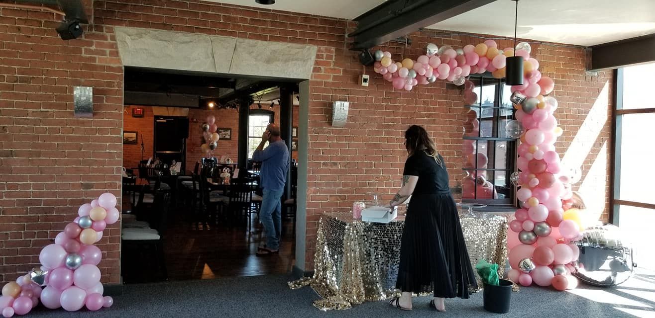 A woman is standing in front of a table decorated with balloons. Free form balloon garland.