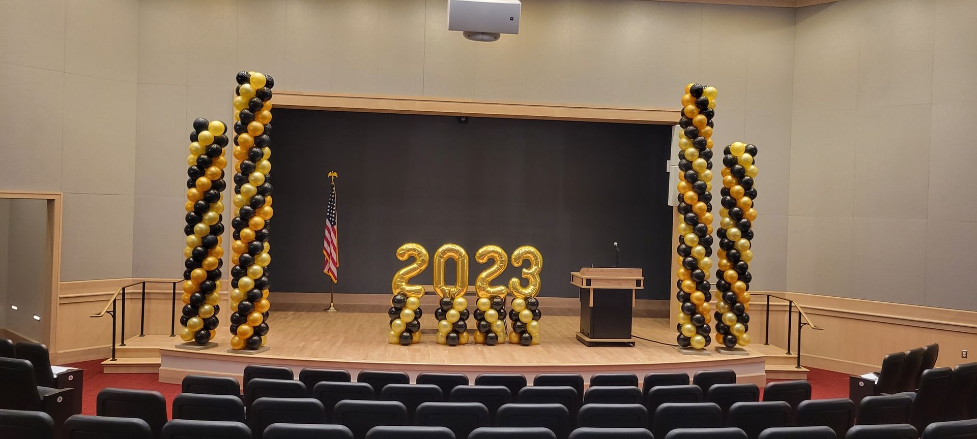 A stage decorated with black and gold balloons for a graduation ceremony.