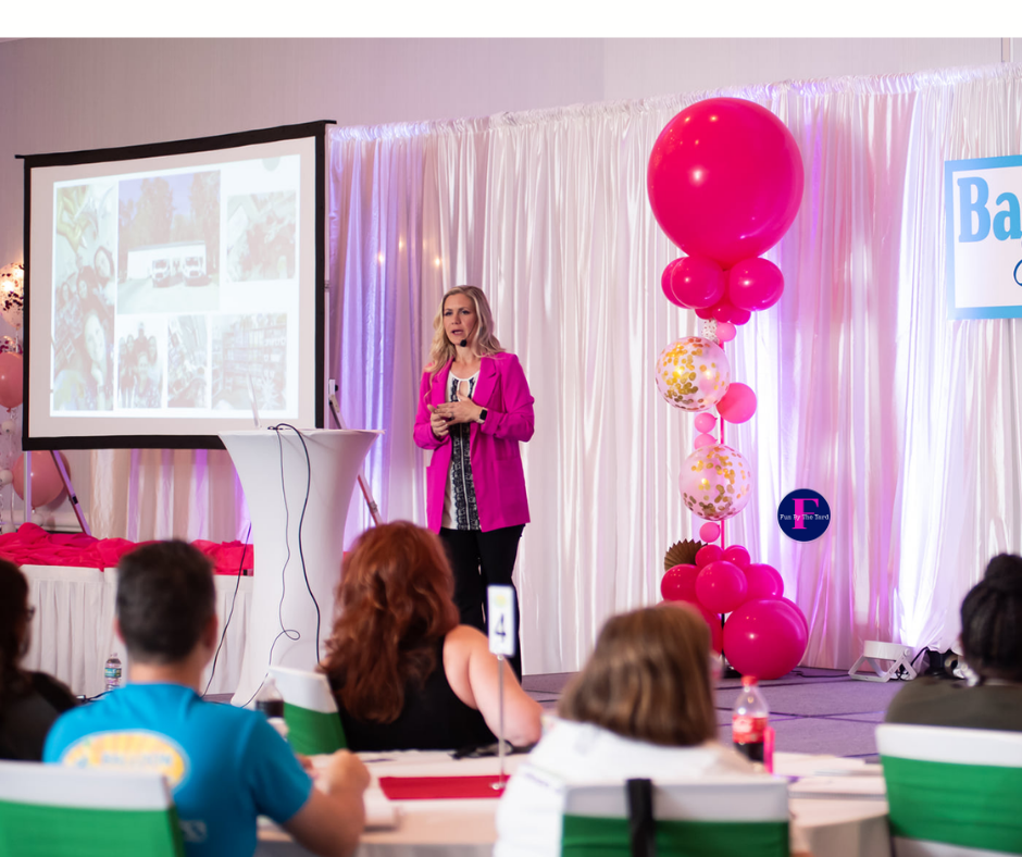A woman in a pink jacket is giving a presentation to a group of people