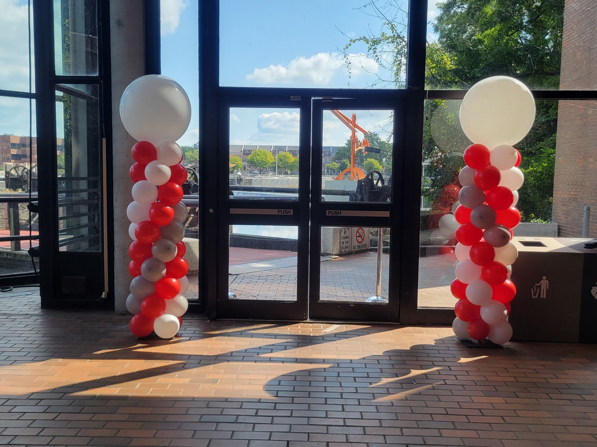 Two balloon columns flank double doors, red, gray, and white balloons. A large white balloon tops each column.