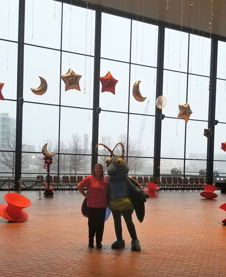 A woman standing next to a mascot in front of a large window