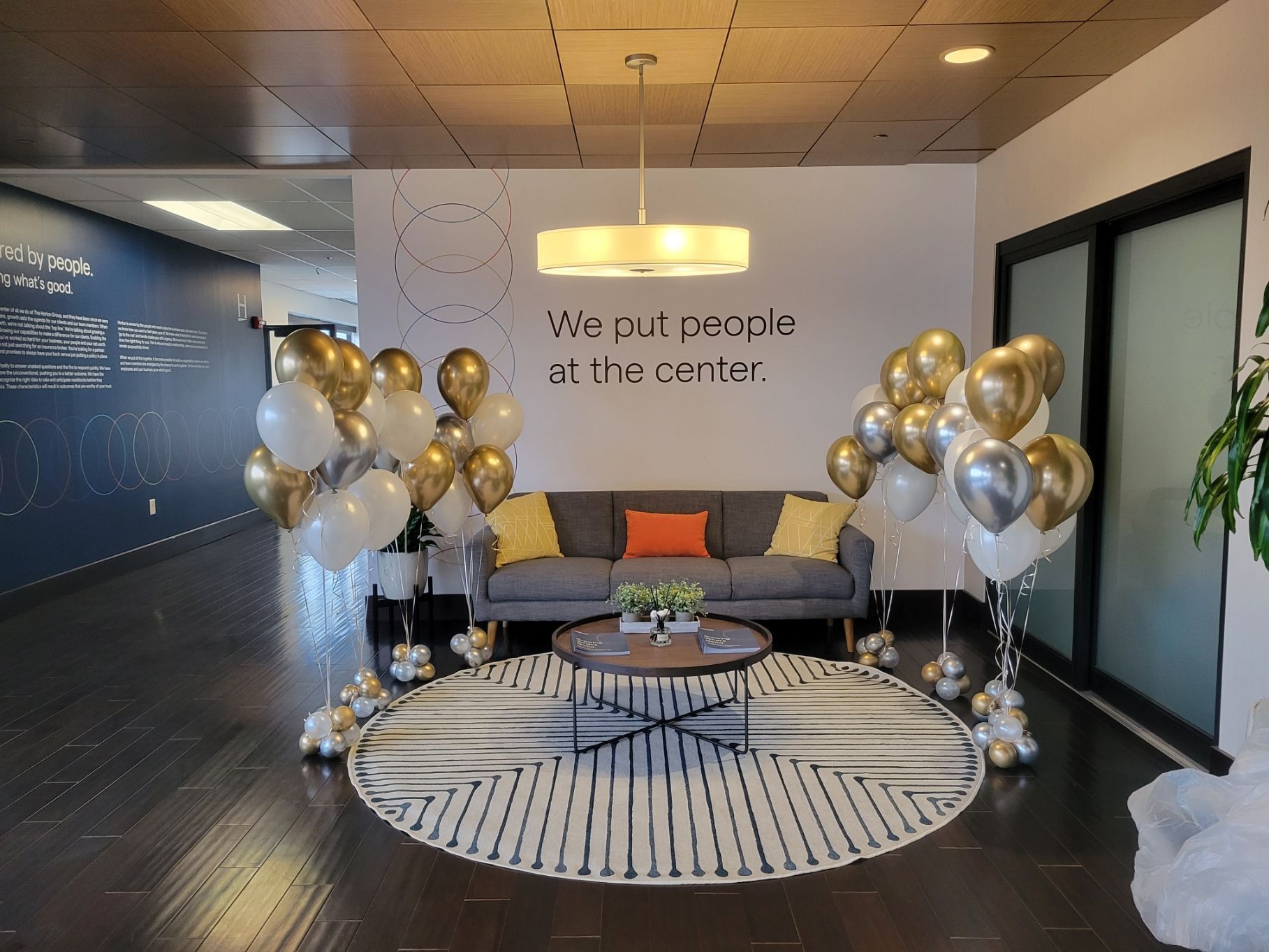 Office reception area decorated with gold and white balloons, sofa, and a round rug.