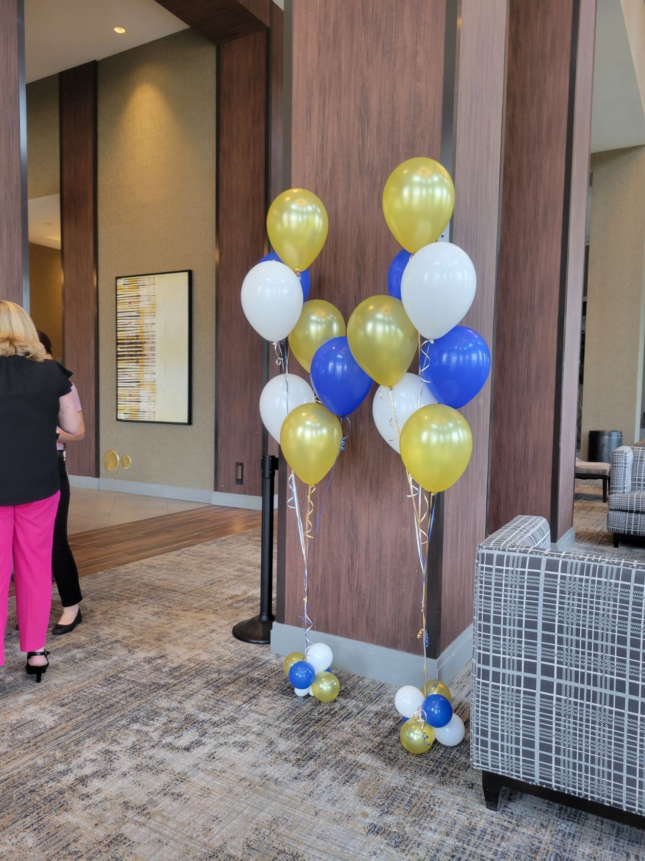 Balloons in gold, blue, and white; two clusters near a brown pillar in a room with a patterned rug.