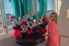 A little girl is standing in front of a table filled with balloons.  Balloon Marquee