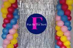 A bunch of colorful balloons are hanging from a silver curtain.