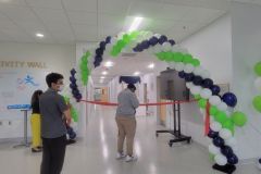 A man is standing under an arch of balloons in a hallway.