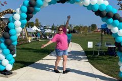 A woman is standing in front of a balloon arch in a park.