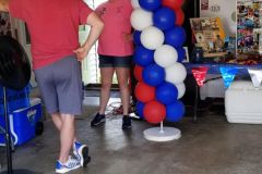 A group of people are standing in a room with red , white and blue balloons.