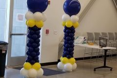 Two columns made of blue , white , and yellow balloons in a room.