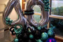A bunch of balloons are sitting on a table in front of a window.  Balloon marquee