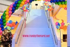 A staircase decorated with balloons and a rainbow arch.
