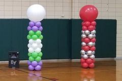 Two balloon columns are sitting on a wooden floor in a gym.