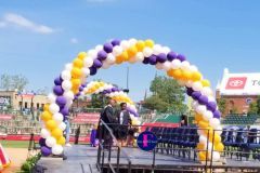 A purple and yellow balloon arch is surrounding a stage for graduation.