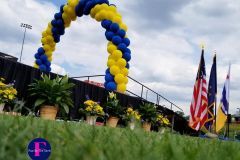 A blue and yellow balloon arch is sitting on top of a lush green field.