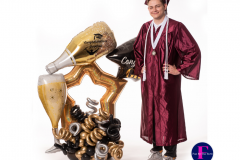 A man in a graduation cap and gown is standing next to a balloon arrangement.