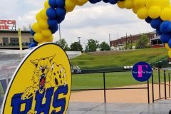 A yellow and blue balloon arch over a baseball field.