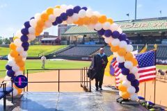 A man in a cap and gown is standing under an arch of balloons on a stage.