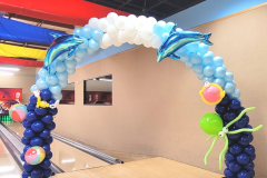 A bowling alley is decorated with balloons and dolphins for under the sea theme.