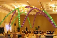 A room filled with tables and chairs decorated with green and purple balloons.