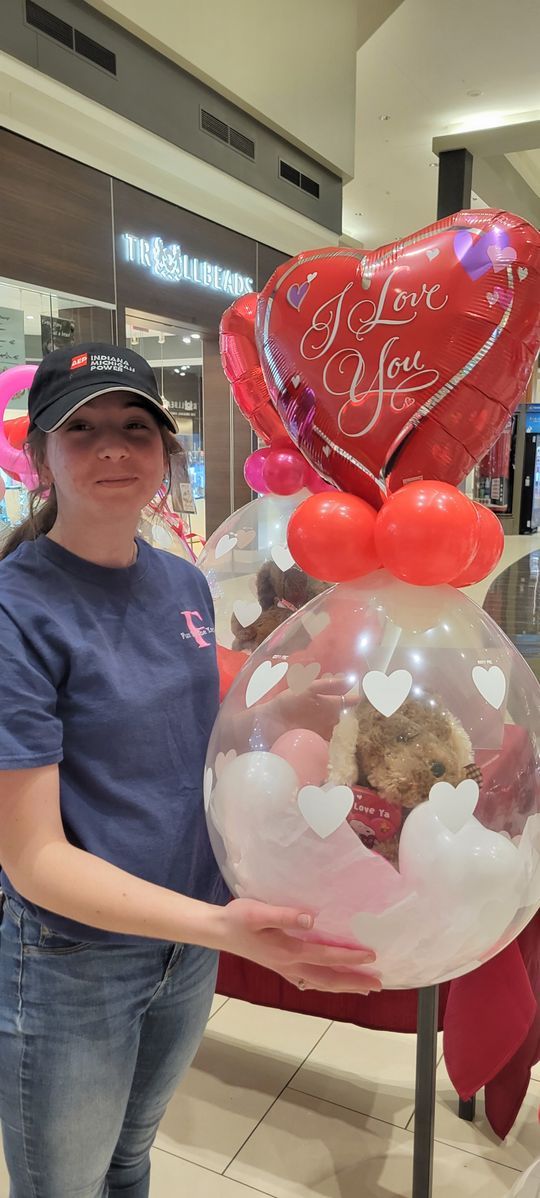 A woman is holding a balloon with a teddy bear inside of it.