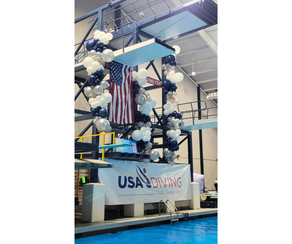 Diving platform decorated with balloons and an American flag. USA Diving banner hangs below, over a pool.