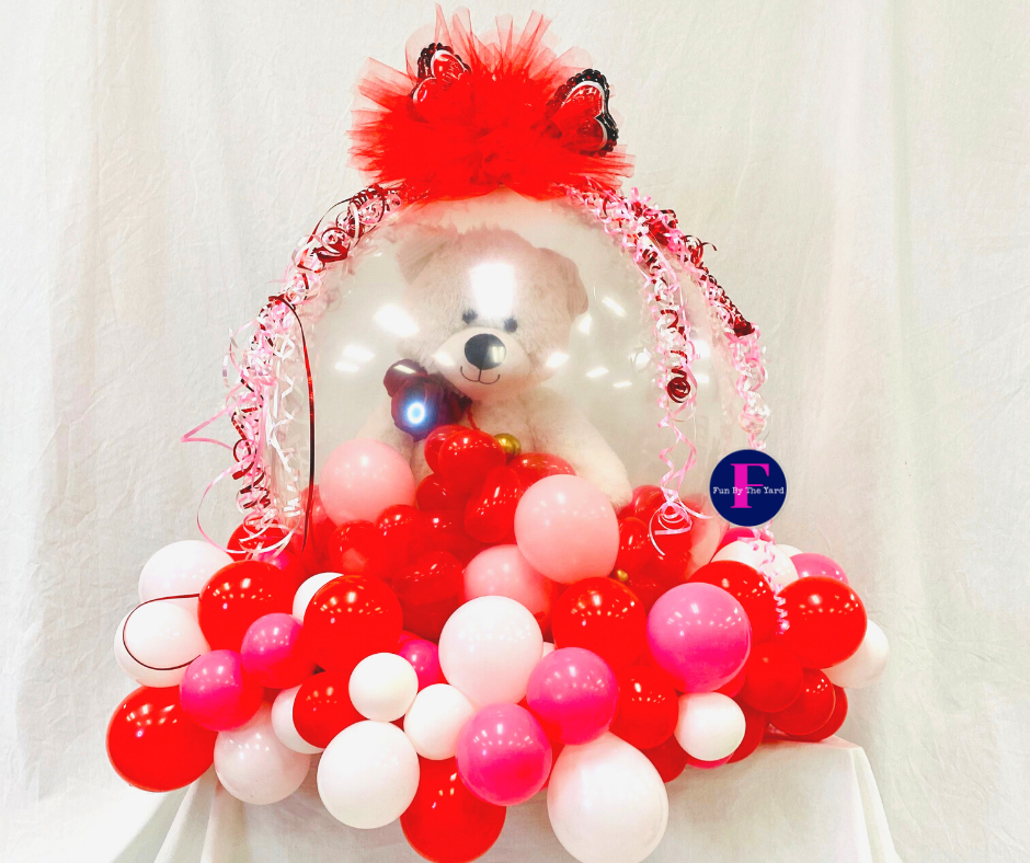 A teddy bear in a balloon surrounded by red and pink balloons