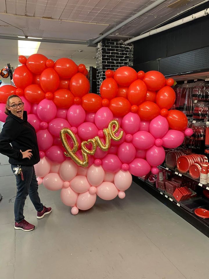A woman is standing in front of a heart made of balloons with the word love on it.