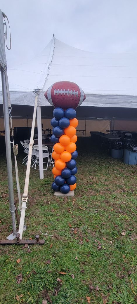 Balloon column with football topper. Blue and orange spiral balloons on grass. Tent in the background.