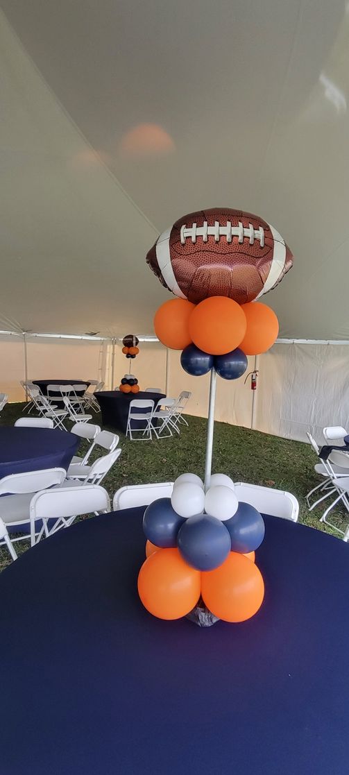 Football balloon centerpiece with orange, navy, and white balloons on a navy tablecloth, outdoor event setting.